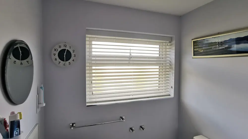 White faux wood Venetian blind in a bathroom, tilted to let in natural light while maintaining privacy