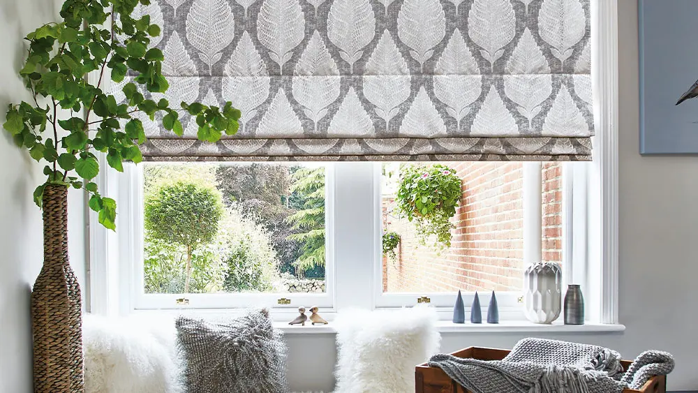 Elegant grey leaf-patterned Roman blind softly folded in a living room window overlooking a garden