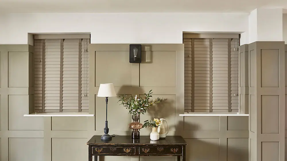 Wooden Venetian blinds in a warm-toned panelled room, tilted to filter soft natural light