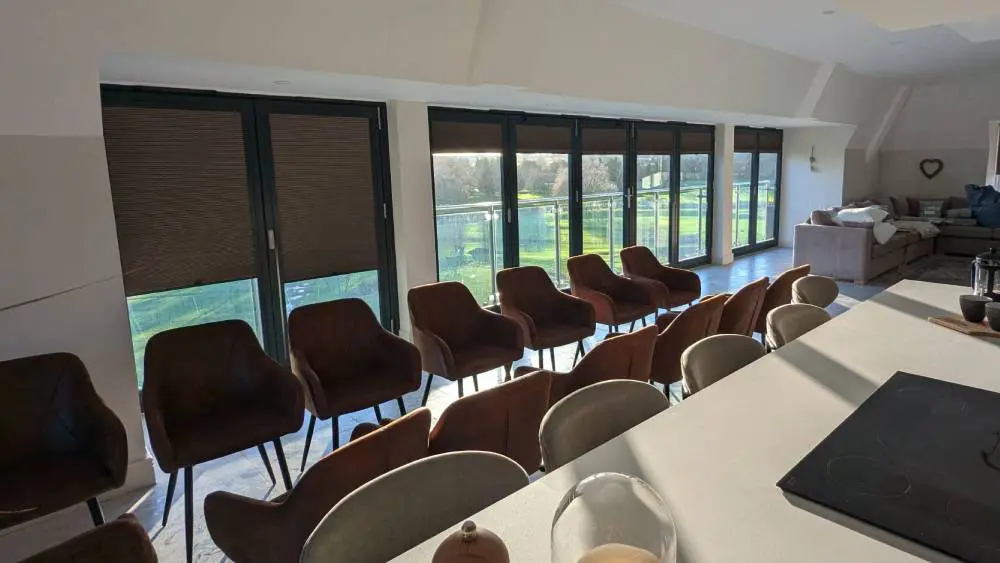 White pleated Perfect Fit blinds clipped into each panel of dark-framed bi-fold doors, looking out onto a garden