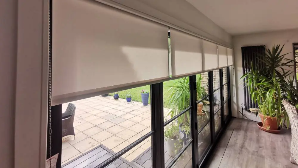 Multiple roller blinds fitted across bi-fold doors with a pelmet cassette, looking out to a garden patio